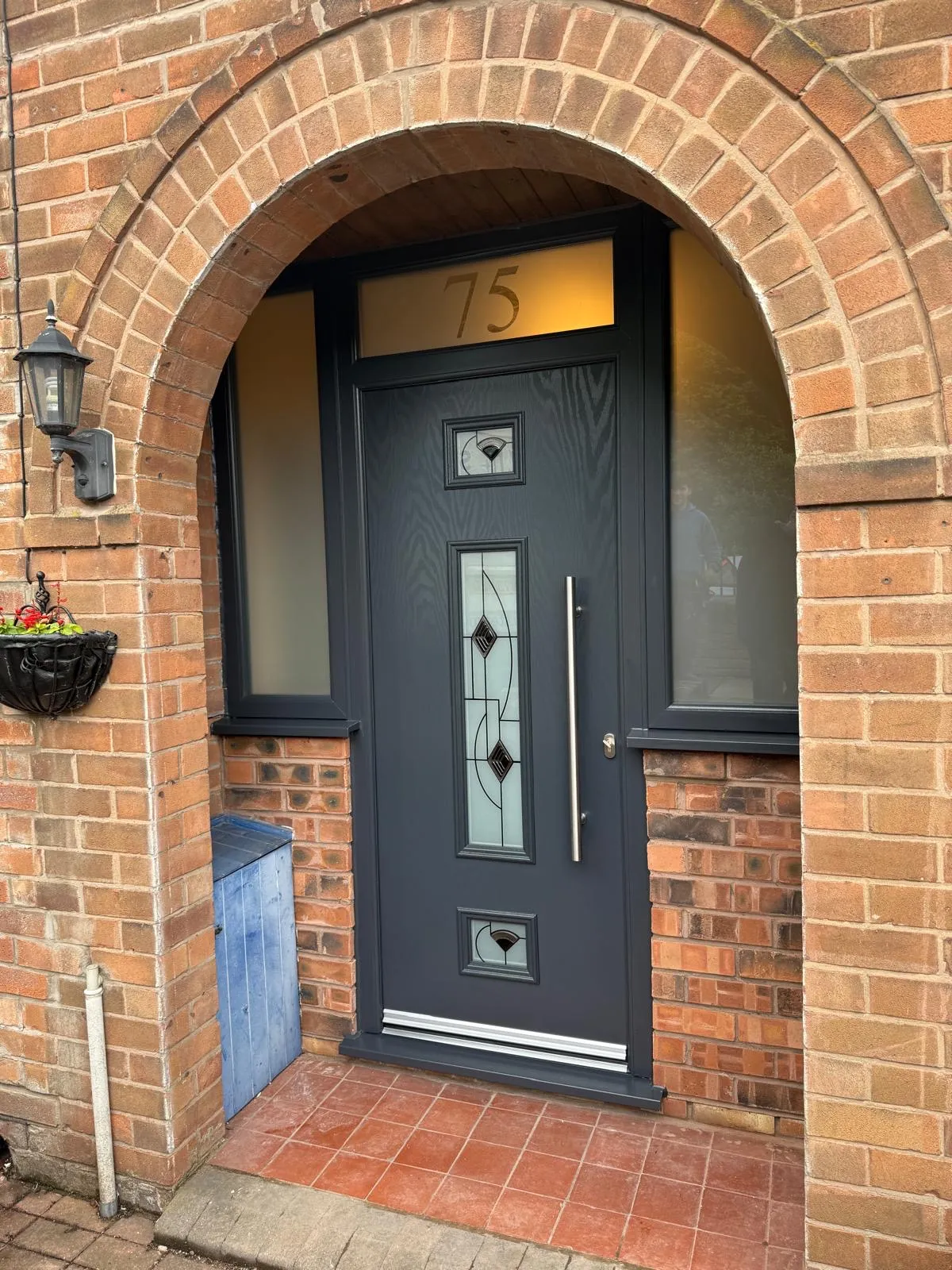 Anthracite grey composite front door with decorative glass panels set within a brick arch.