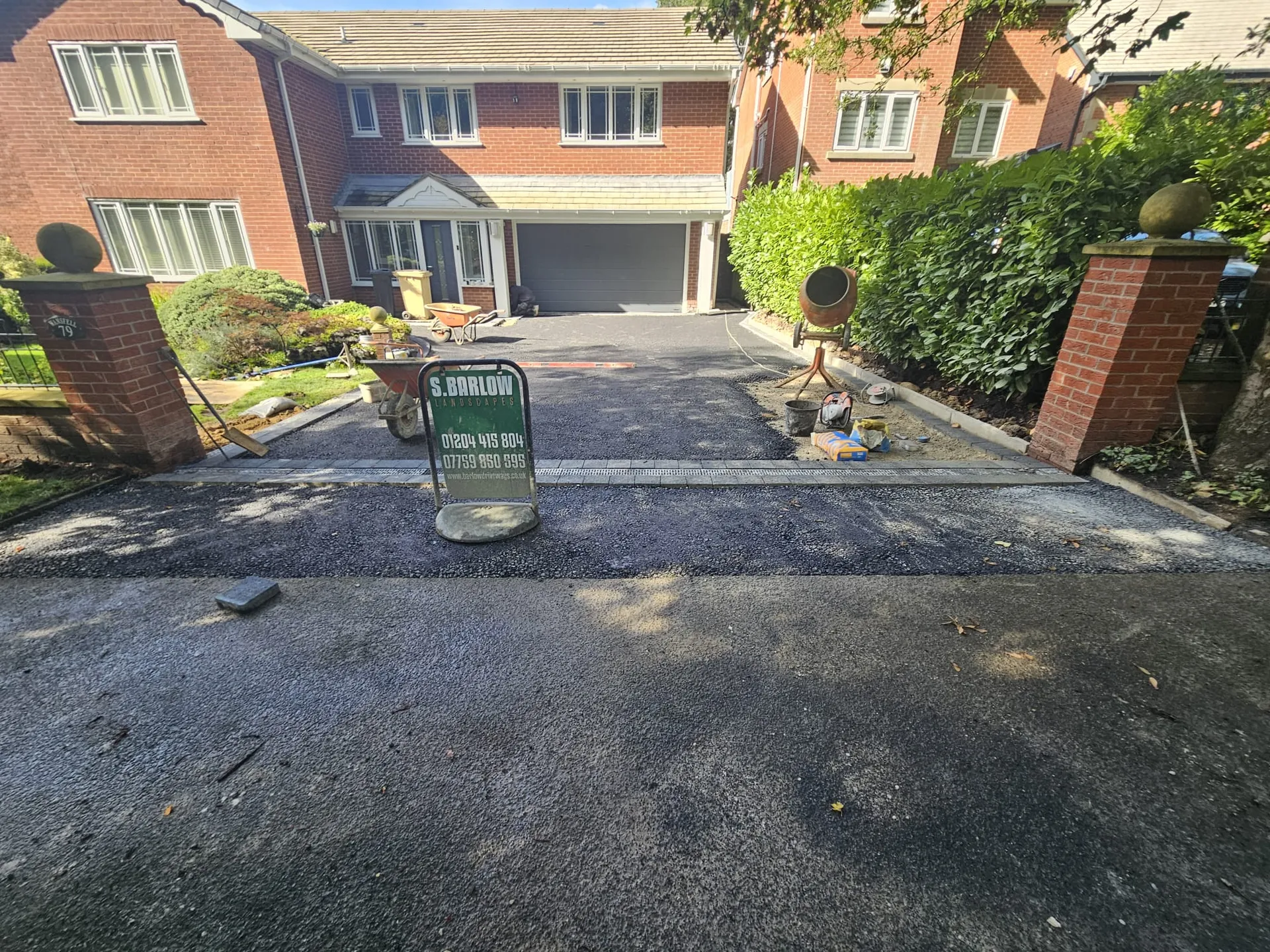 Residential tarmac driveway installation in Bolton leading to brick houses with garages — Barlow Landscapes