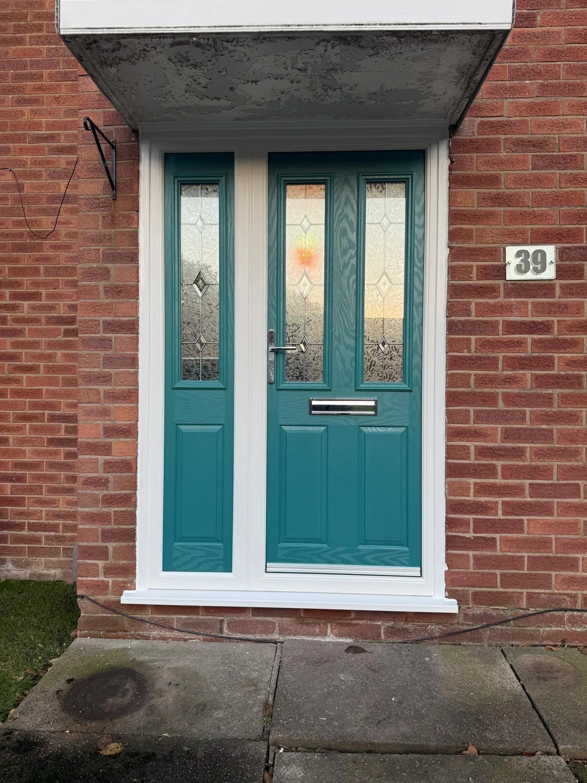 Teal composite front door with decorative frosted glass panels on a red brick house.