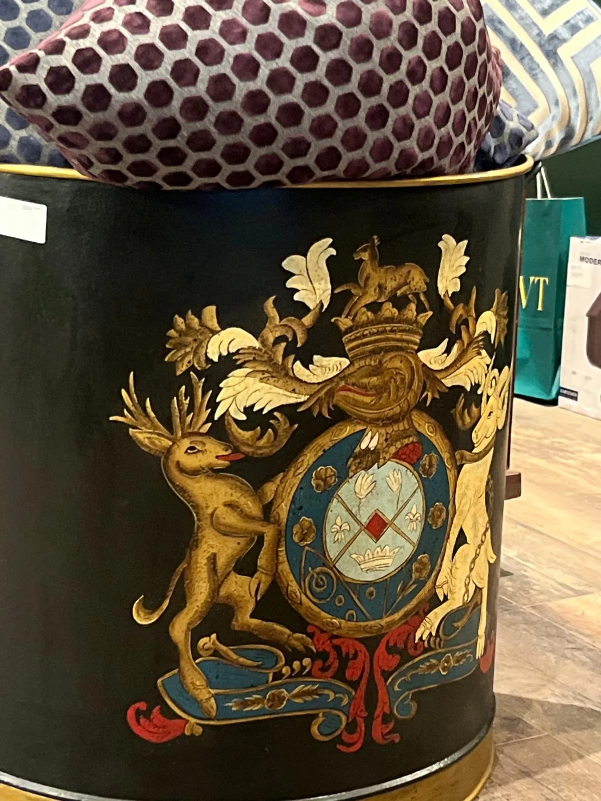 A cylindrical black container with ornate gold heraldic crest featuring a deer and crown, topped with patterned fabric.