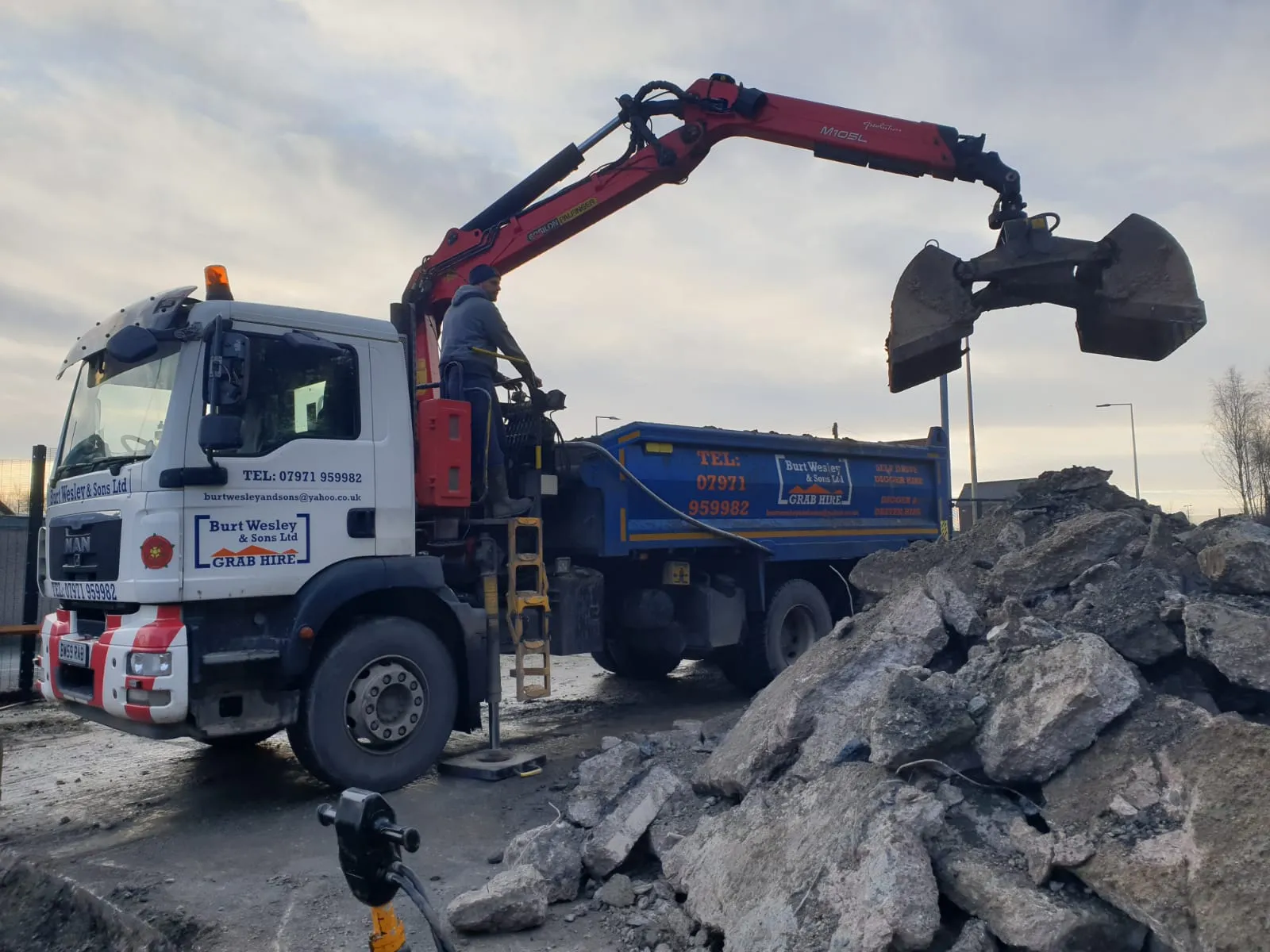 Excavator and truck working on construction site with large rocks and debris