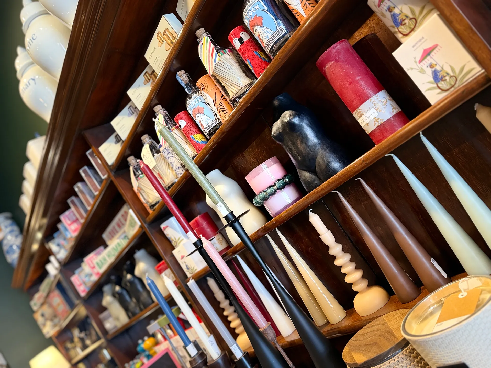 Wooden shelves displaying various colored candles, bottles, and decorative items arranged in rows.