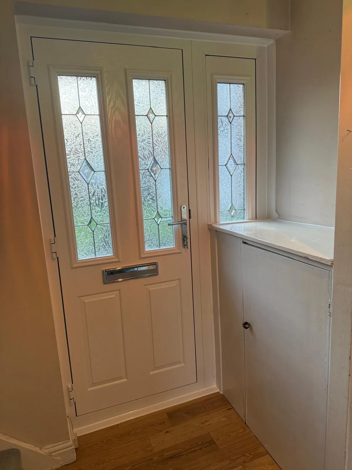 White composite front door with decorative frosted glass panels and sidelight, interior hallway view.