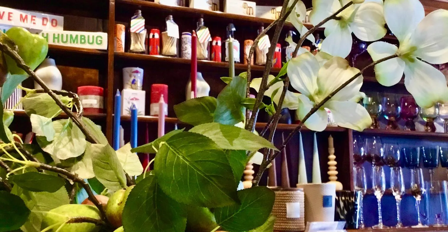 A retail display shelf with beauty products, candles, and decorative flowers, featuring white orchids in the foreground
