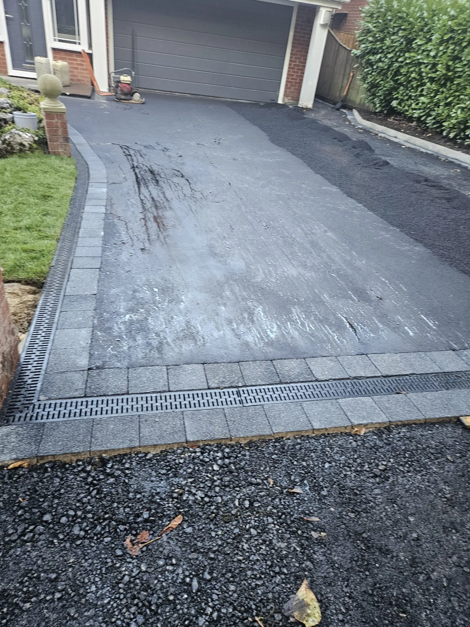 Dark asphalt tarmac driveway Bolton with grey paving stone border and drainage grates — Barlow Landscapes