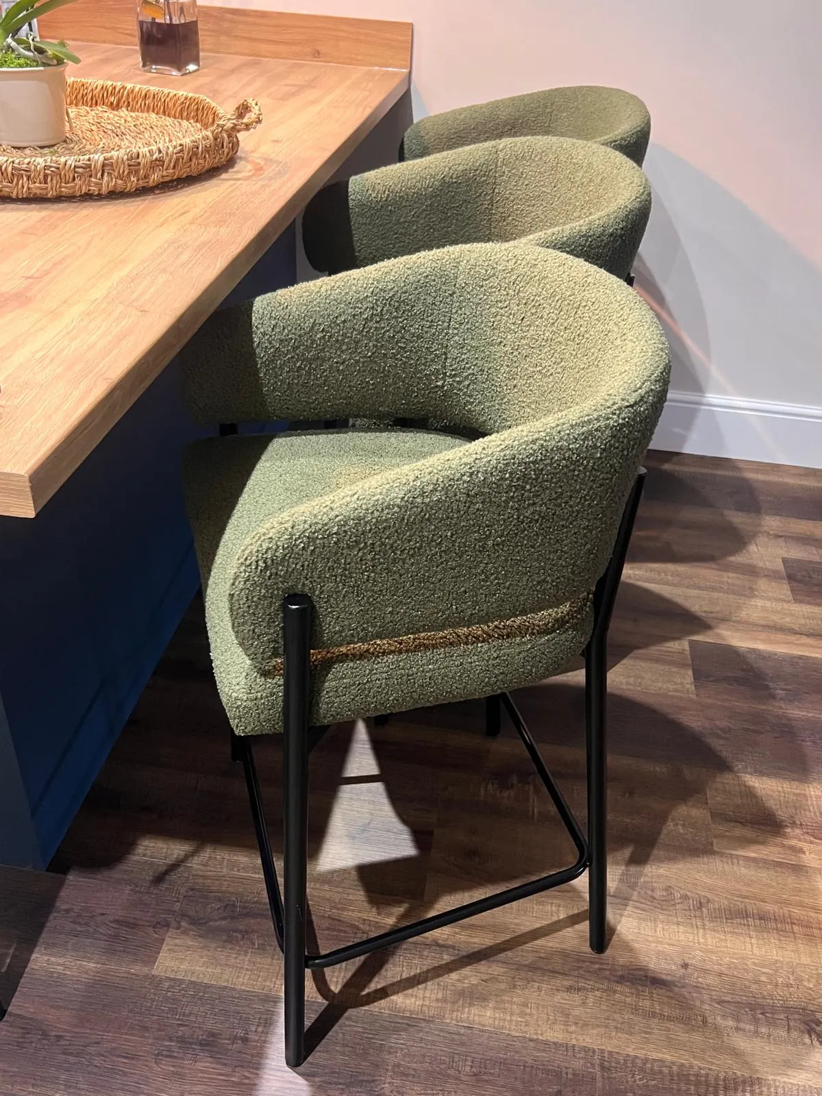 Three green upholstered bar stools with black metal legs positioned at a wooden counter.