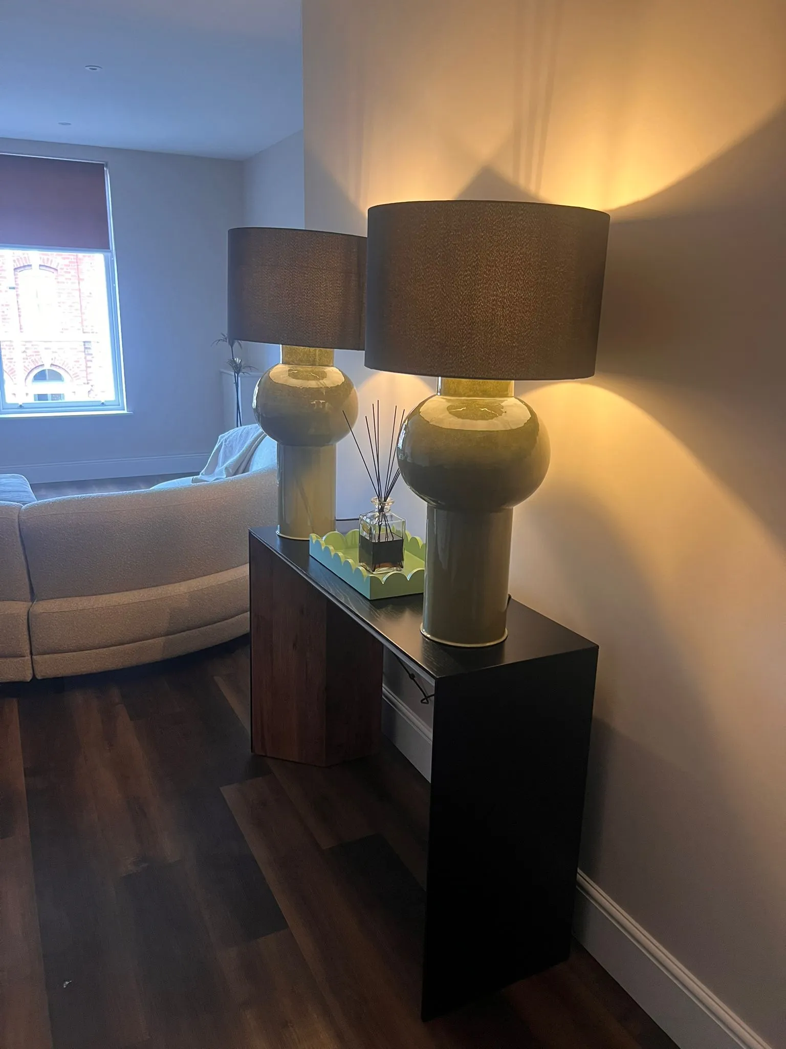 Interior scene showing elegant table lamps with dark lampshades on a black console, next to cream sofas in a sophisticated living room setting.