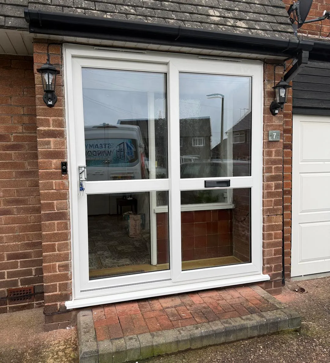 White double French doors with glass panes on a brick house exterior, flanked by a garage door on the right.