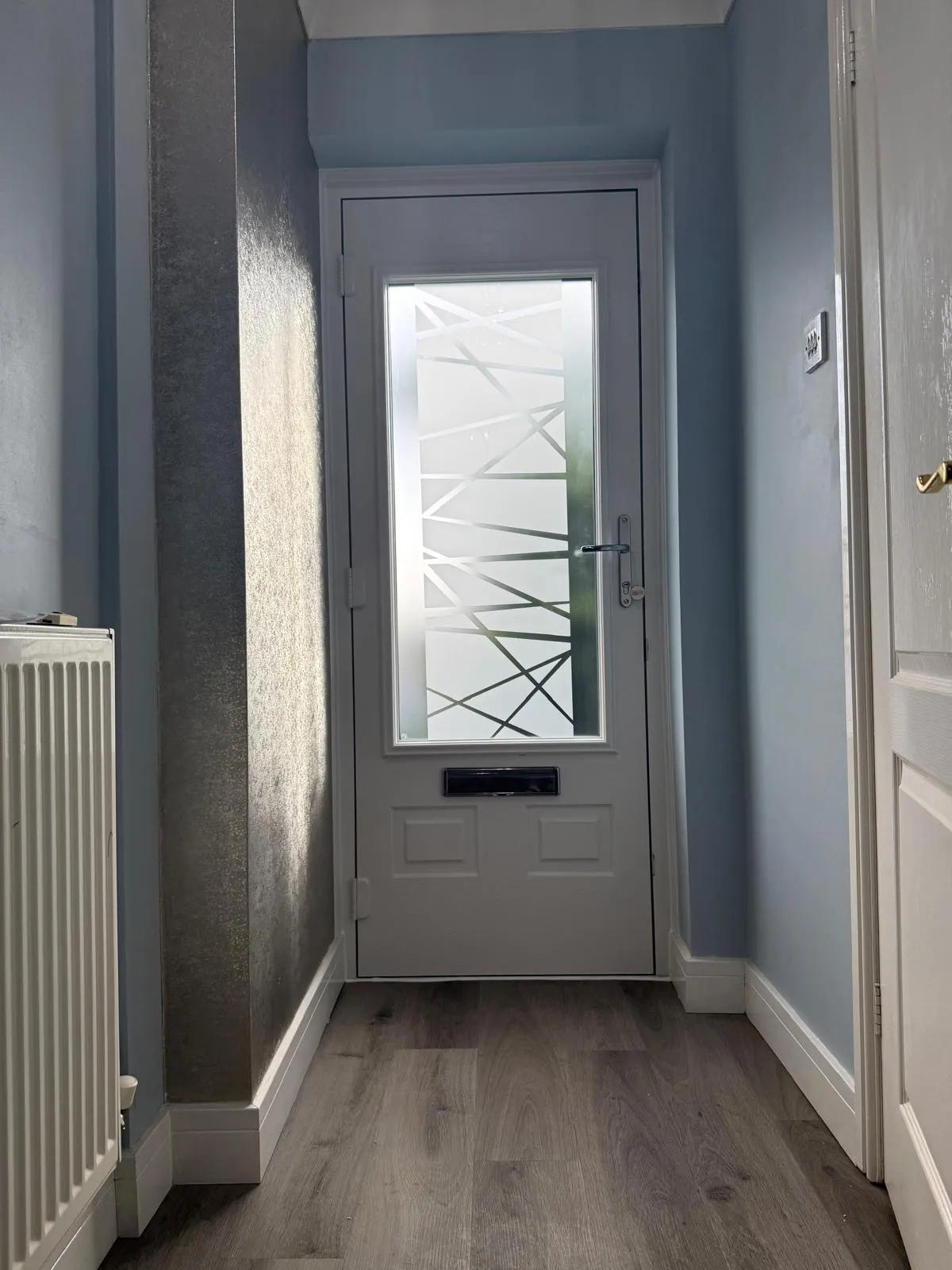 Grey composite door with frosted geometric glass panel in a blue-walled hallway.