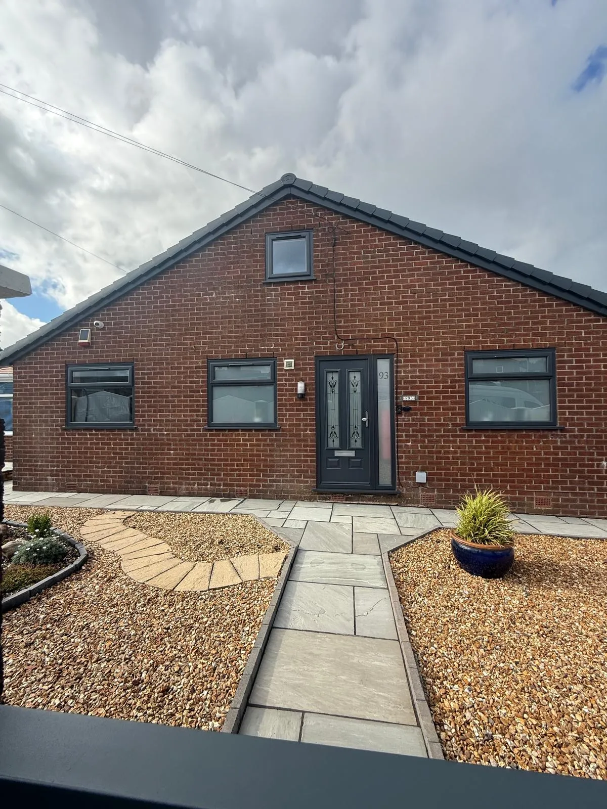 Anthracite grey composite front door with decorative leaded glass panels on a bungalow with landscaped front garden.
